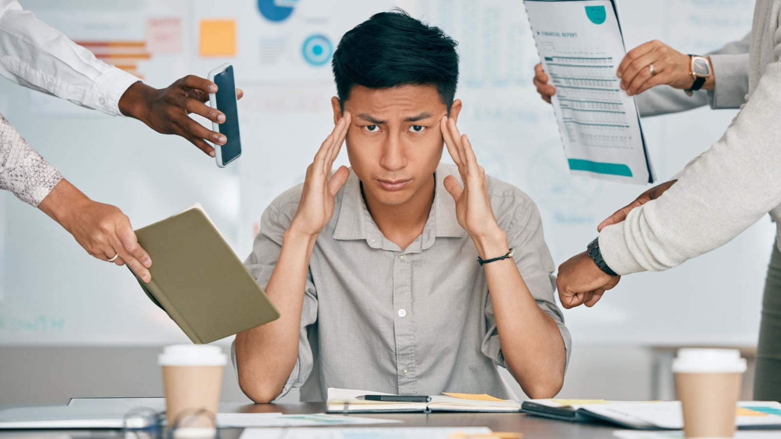 An overwhelmed man at work with lots of people and tasks competing for attention to represent the productivity hacks that do more harm than good.