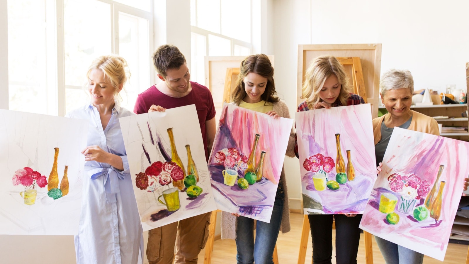 A group of art class students hold up their still life paintings. Each is unique, showing the individual talents and artistic interpretation. 