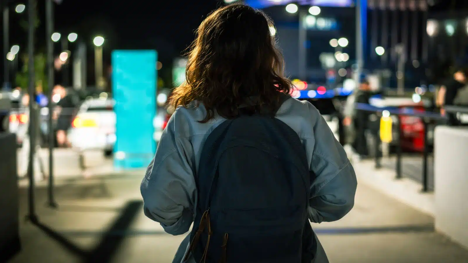 Back view of a woman walking in a city along at night to represent street smarts.