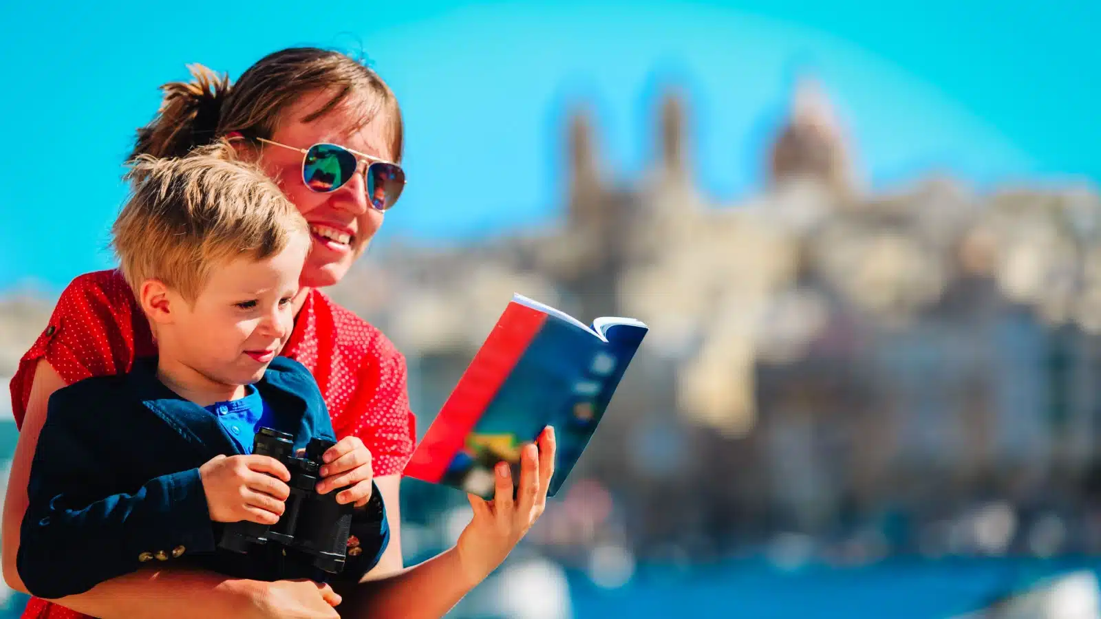 A tourist holds her young son while looking at a travel guide book.