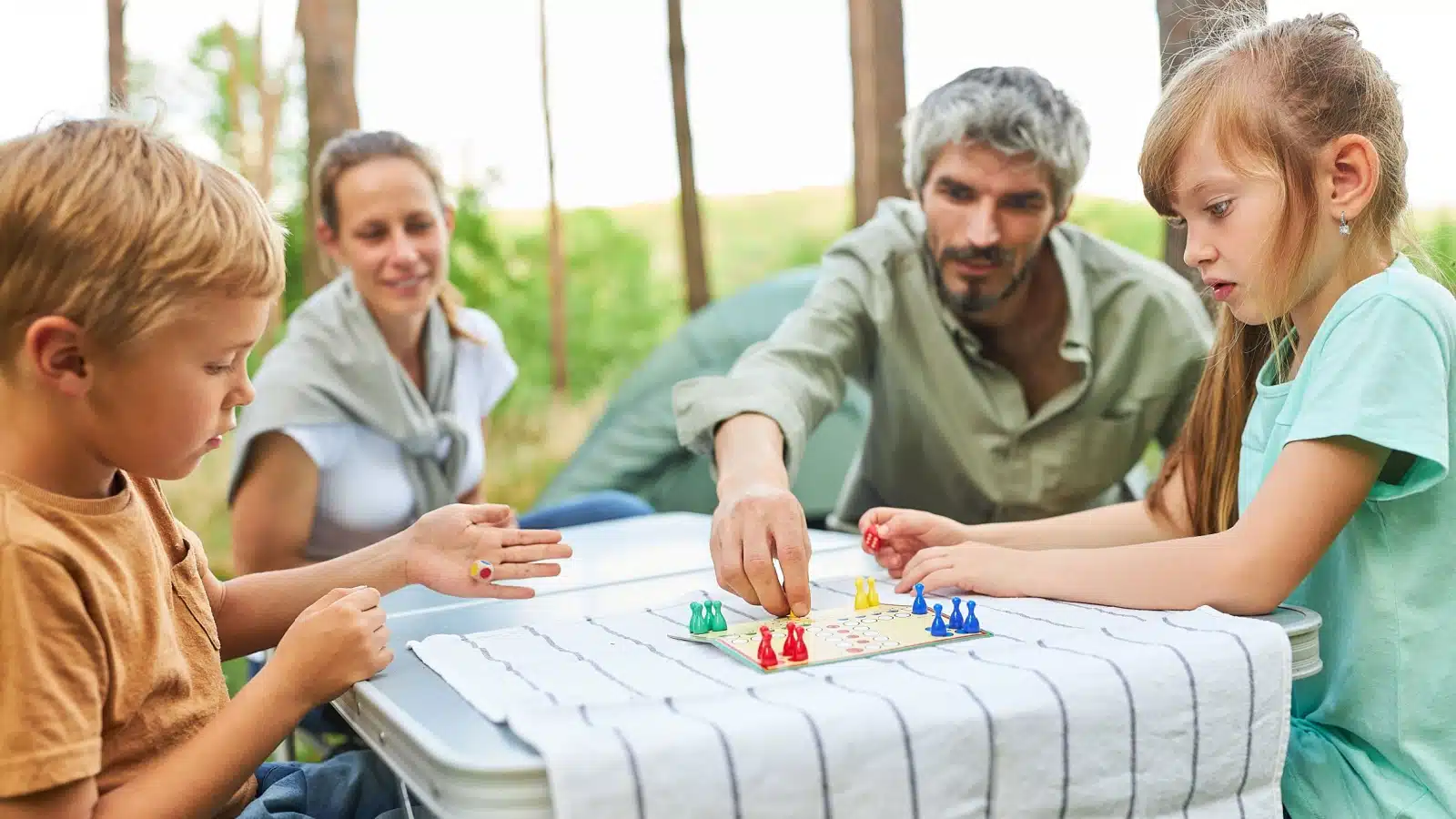 A family plays a travel-sized board game outside.