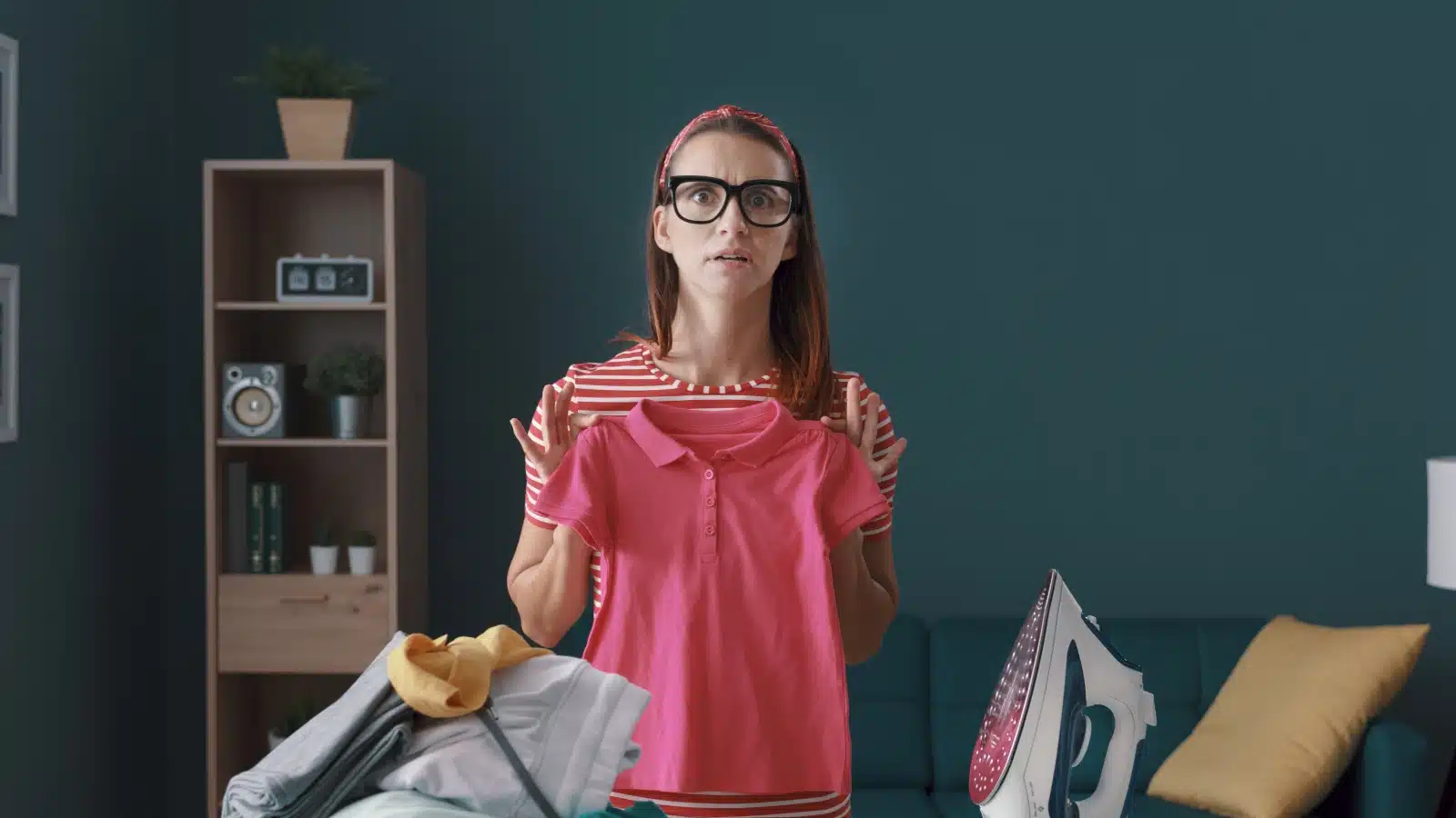 A disappointed woman holds up her shrunken shirt after her husband attempted to do laundry. The image represents weaponized incompetence.