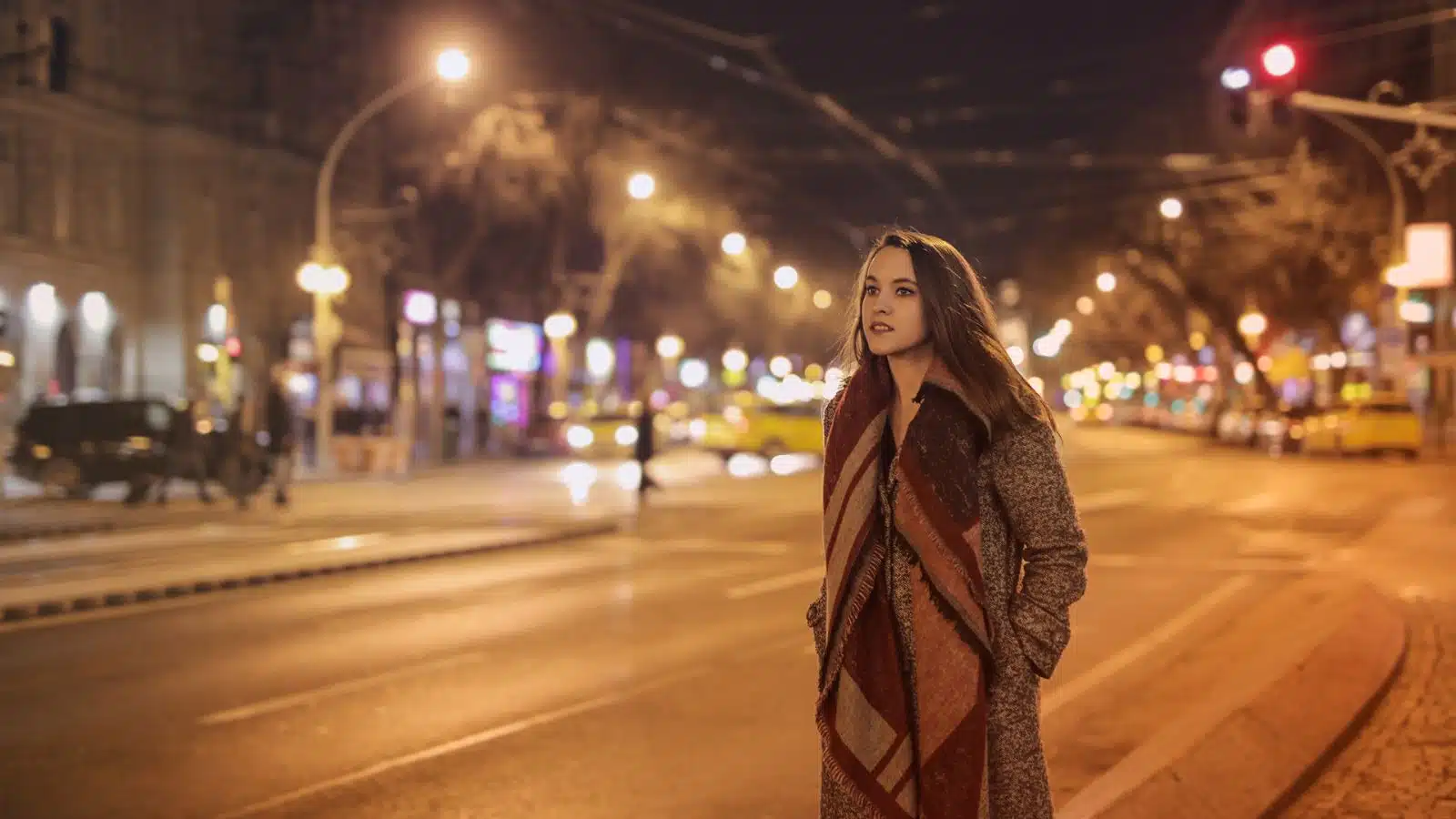 A woman walking on a city street alone at night.