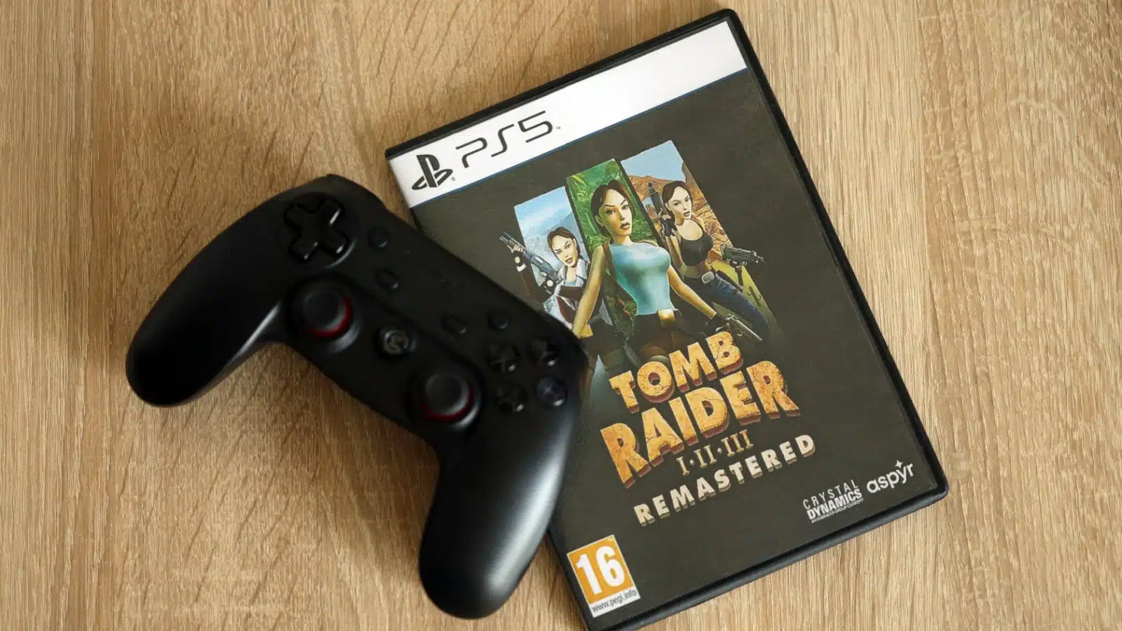 A PlayStation controller sits on top of a case for the remastered Tomb Raider series for PS5.