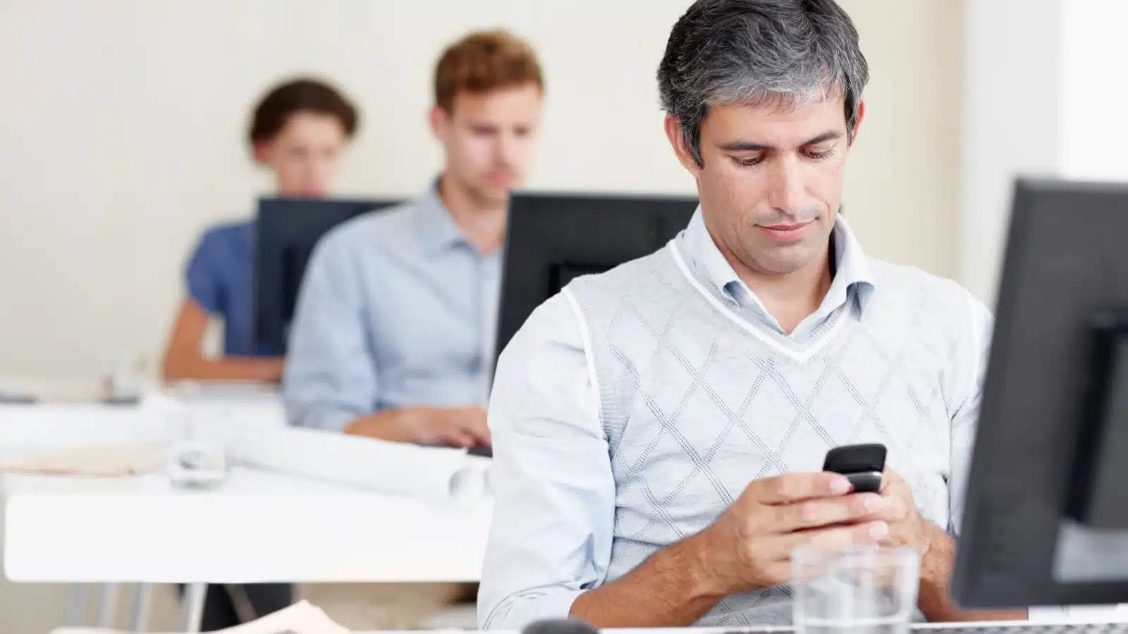 A man looks at his cell phone instead of his work computer.