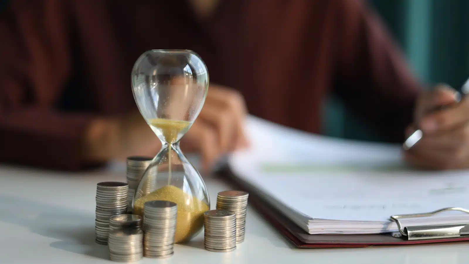 Coins surround a tiny hour glass to represent how a small amount can grow when invested over time.