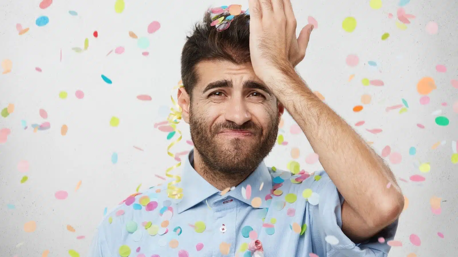 A man slaps his head in frustration as birthday confetti falls down to show that he's forgotten a birthday.