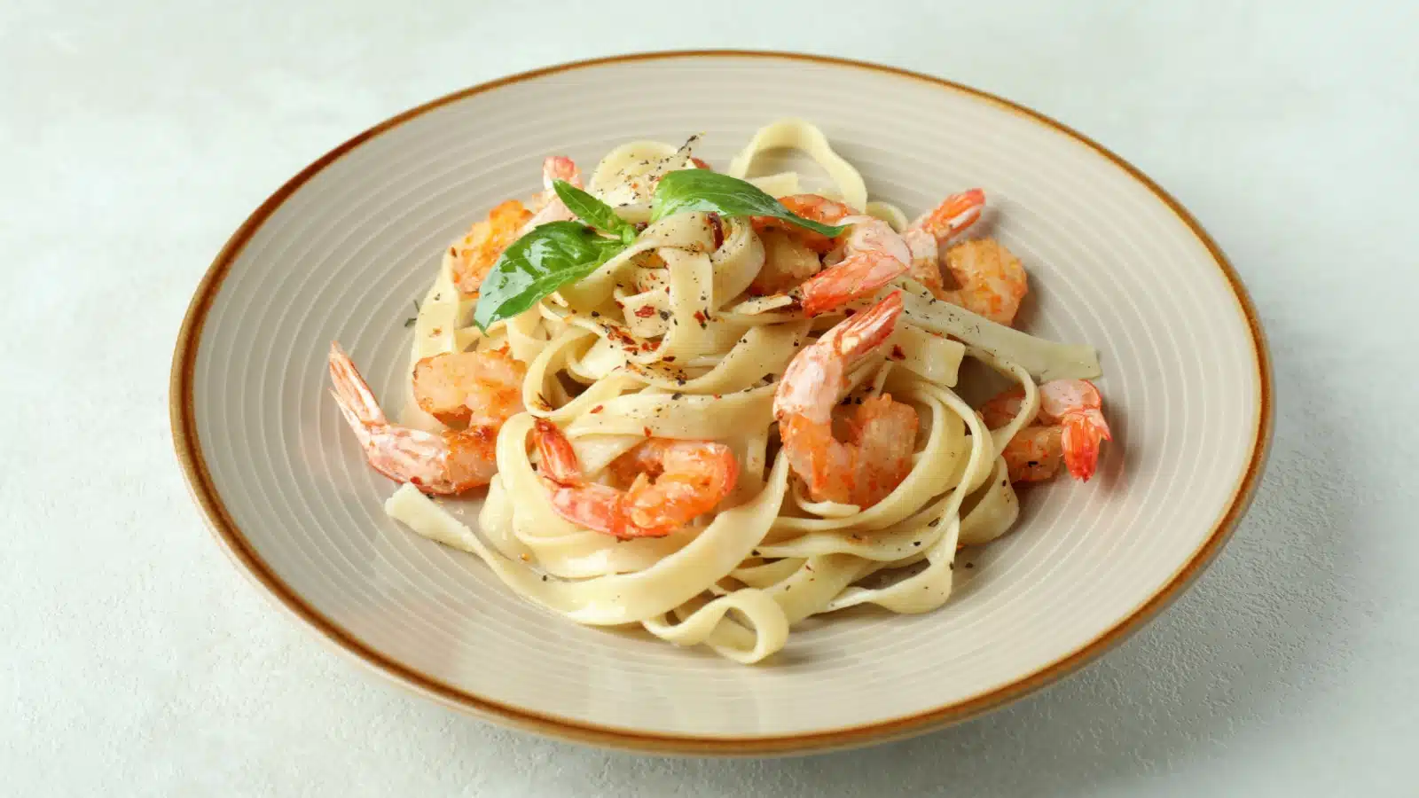 A bowl of shrimp and pasta that is aesthetically pleasing with the shrimp tails on.