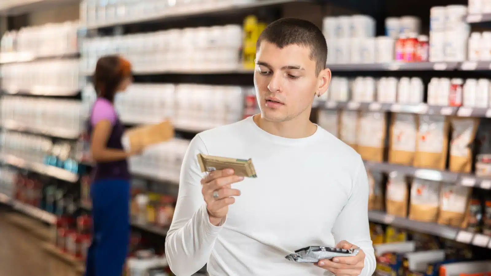 A man looks at the label of a sports bar while grocery shopping.