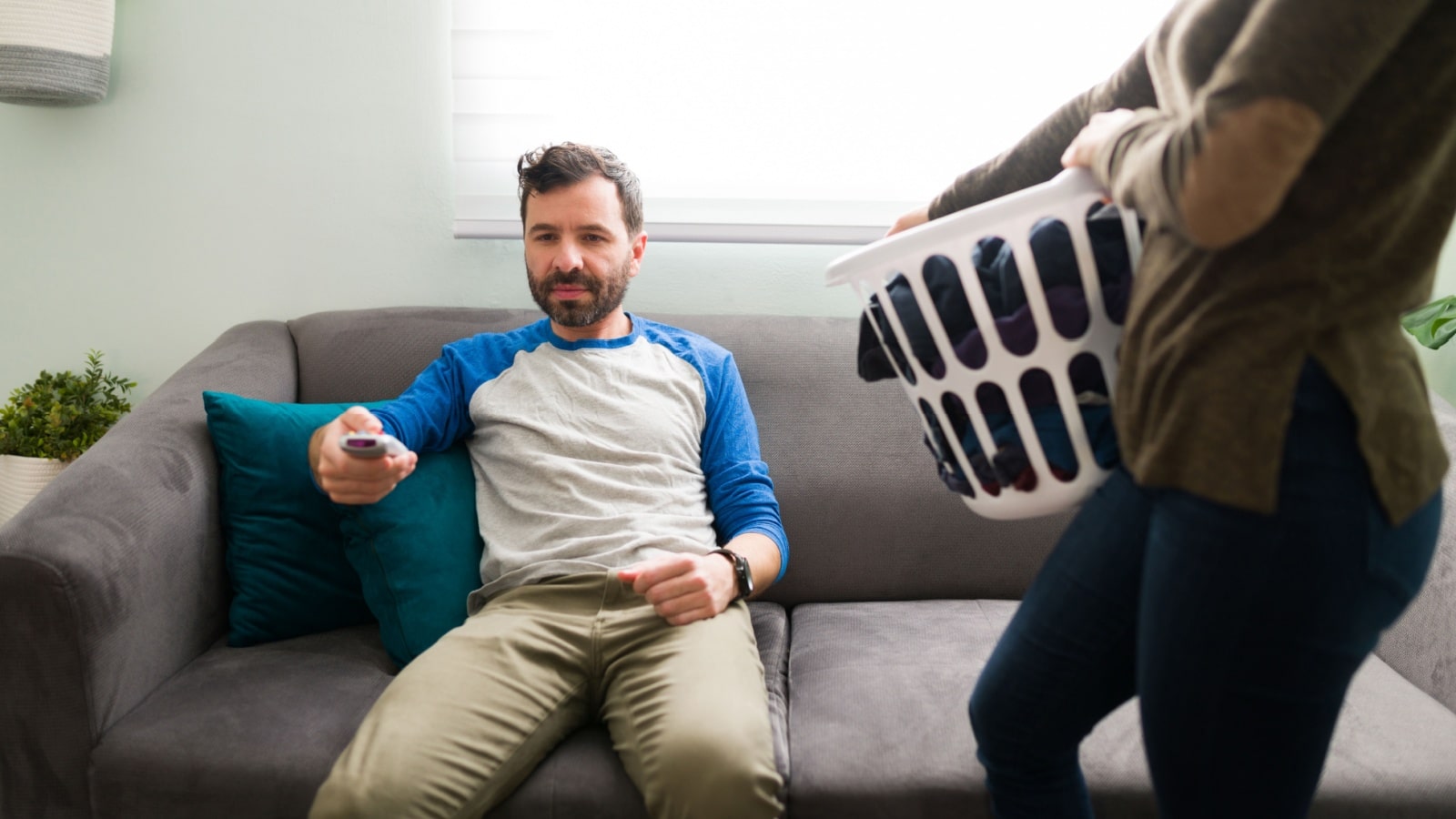 A woman holds a laundry basket while her husband watches television to represent fair play.