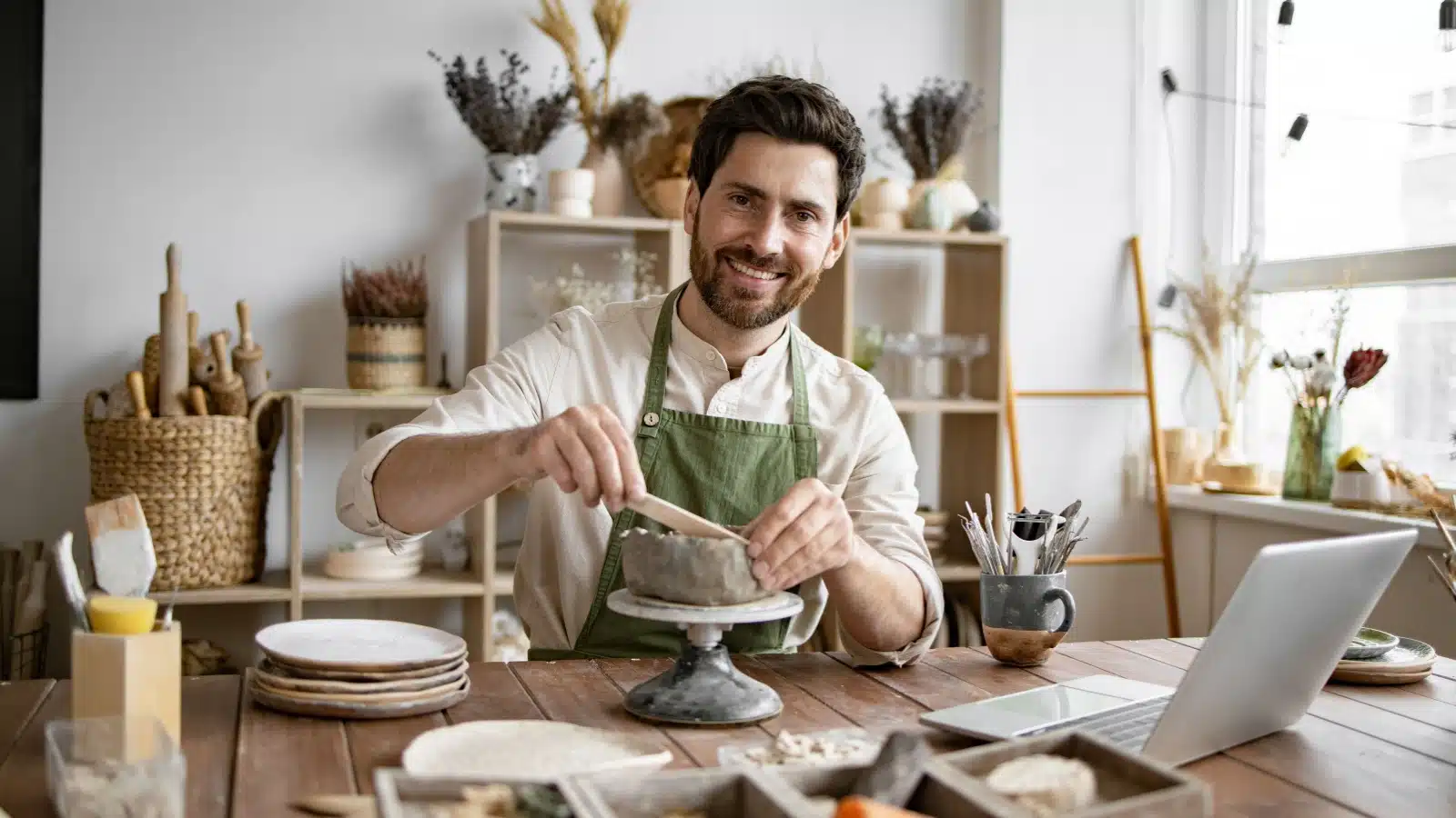 A smiling man works with clay to create pottery, representing one of the creative art hobbies you can explore.