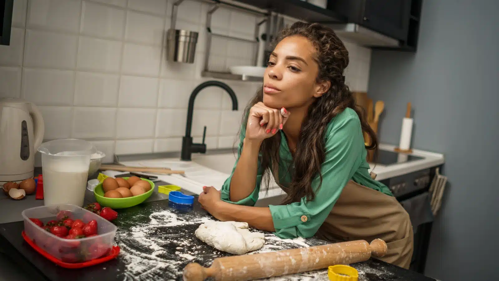 A woman spaces out while she's supposed to be rolling dough for a meal.