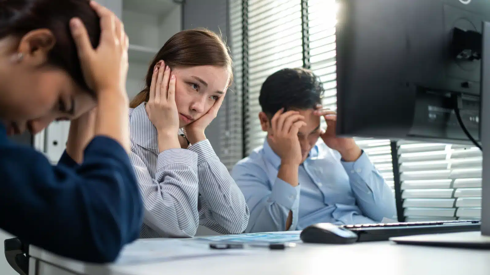 Three bored coworkers gather around a monitor, participating in an endless meeting, to represent one of the biggest time wasters at work.