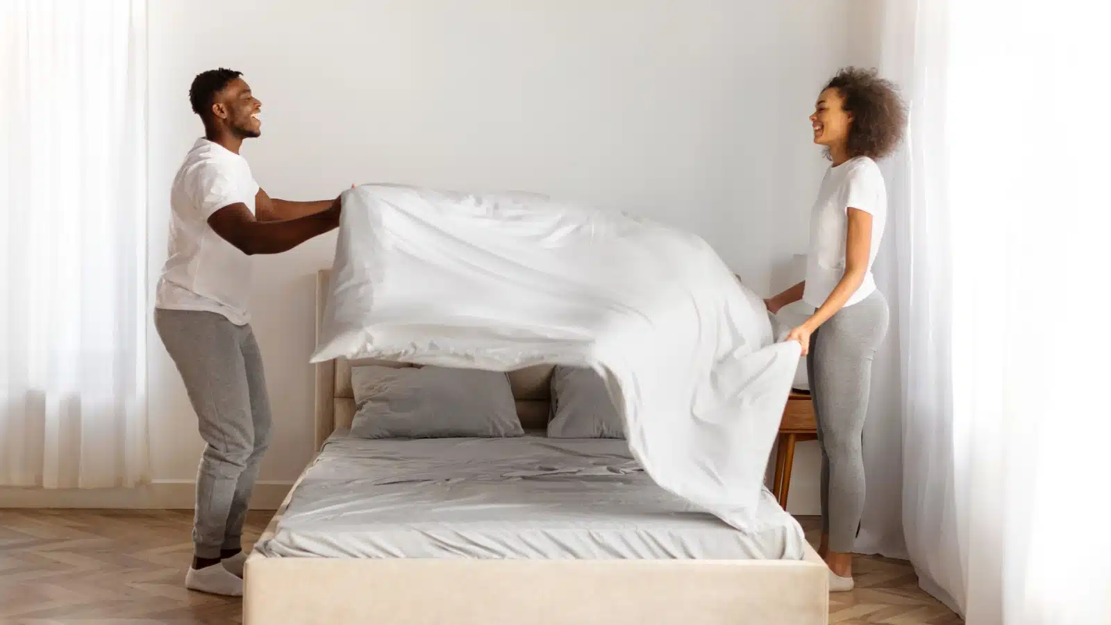 A happy couple makes the bed together in the morning.