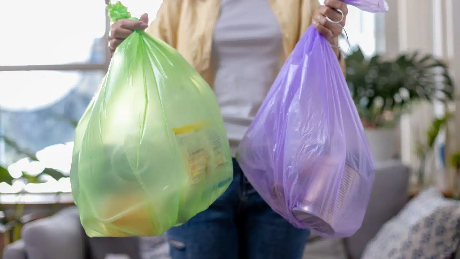 A woman holding colorful kitchen trash bags filled with waste.