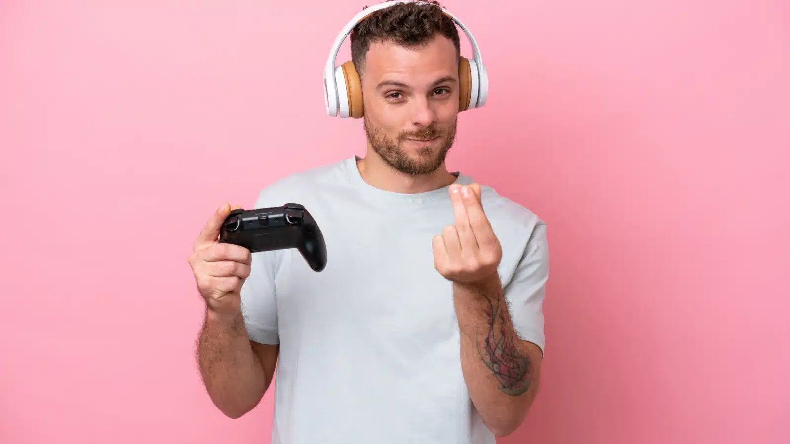 A man on a pink background holds a gaming controller in one hand while making the money gesture with the other, to represent making money playing video games.