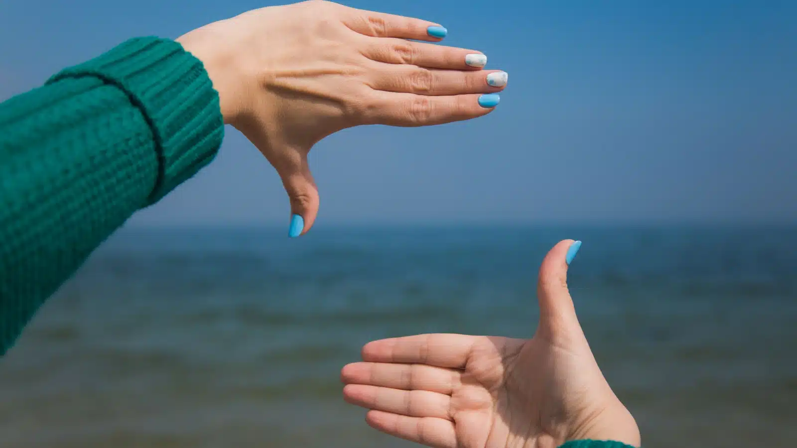 Close up of a woman's hands taking a mental image of the pretty water in front of her.