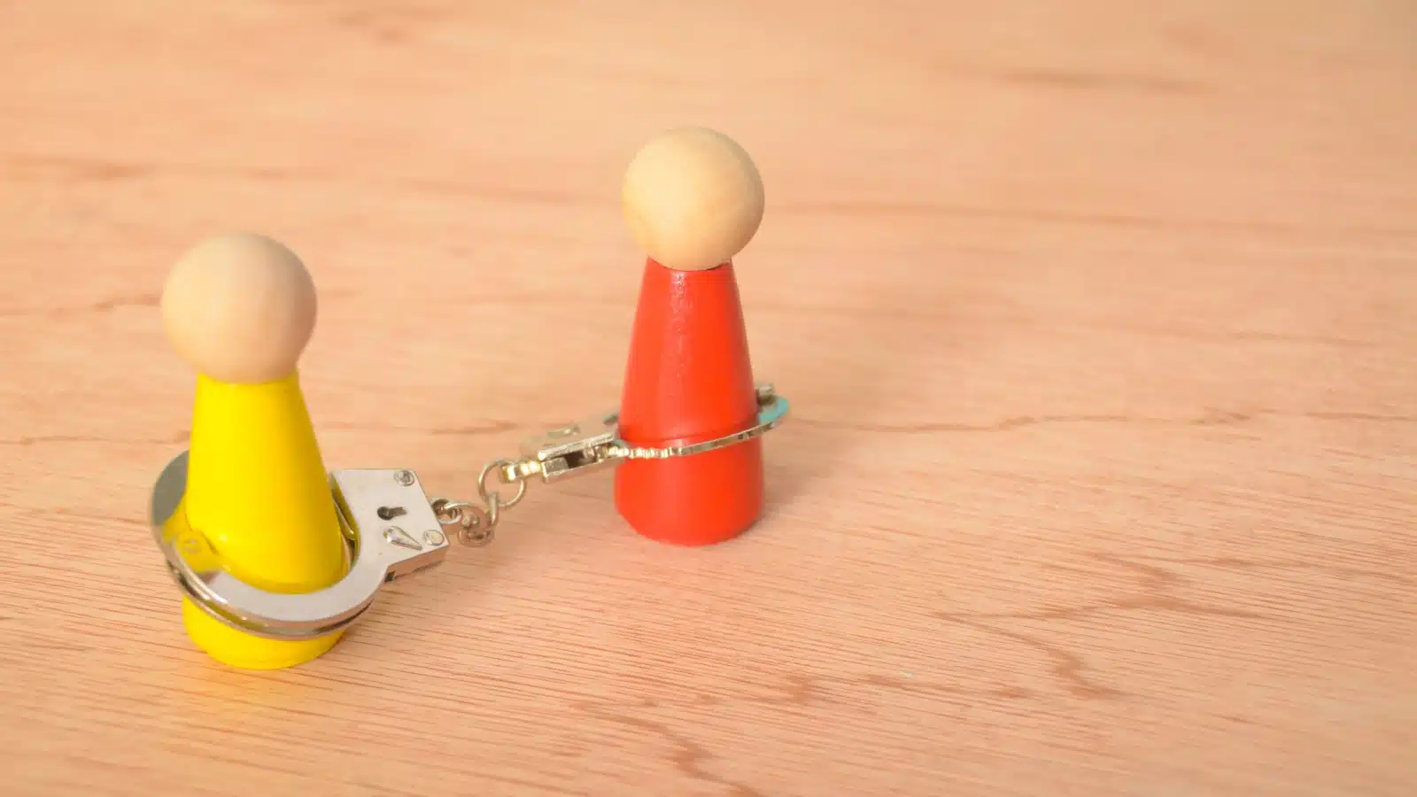 Two small wooden figures are handcuffed together, to represent an obligation.