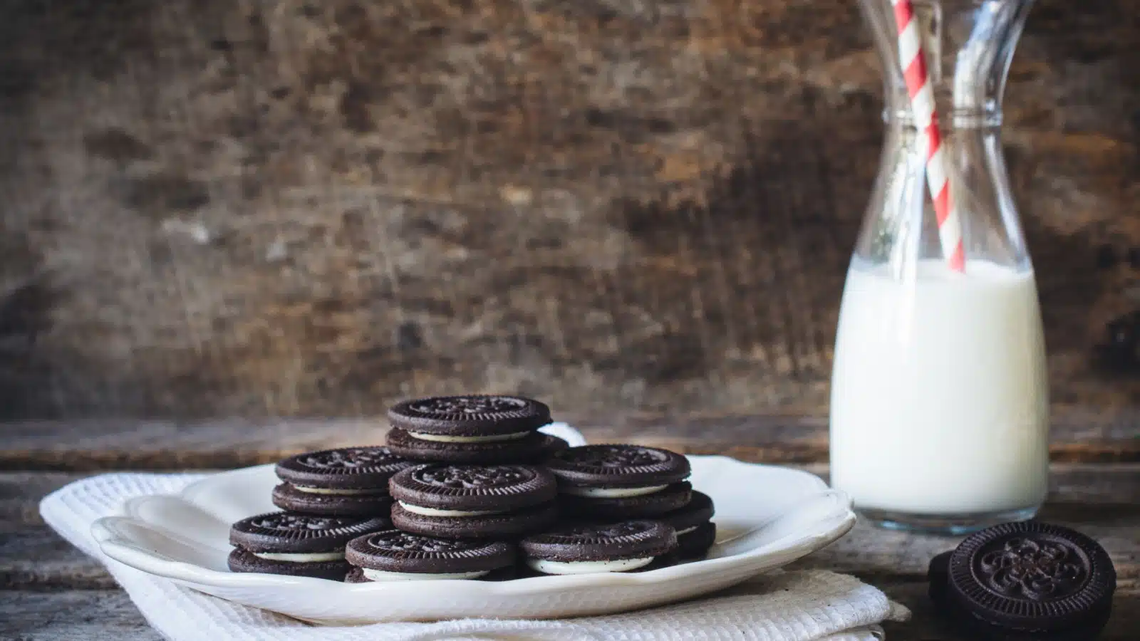A plate of black & white sandwich cookies next to a bottle of milk on a table.