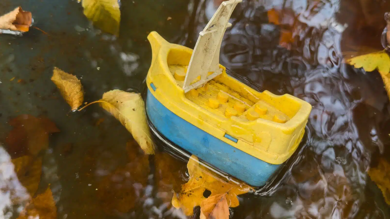 An old toy boat washed up in a puddle.