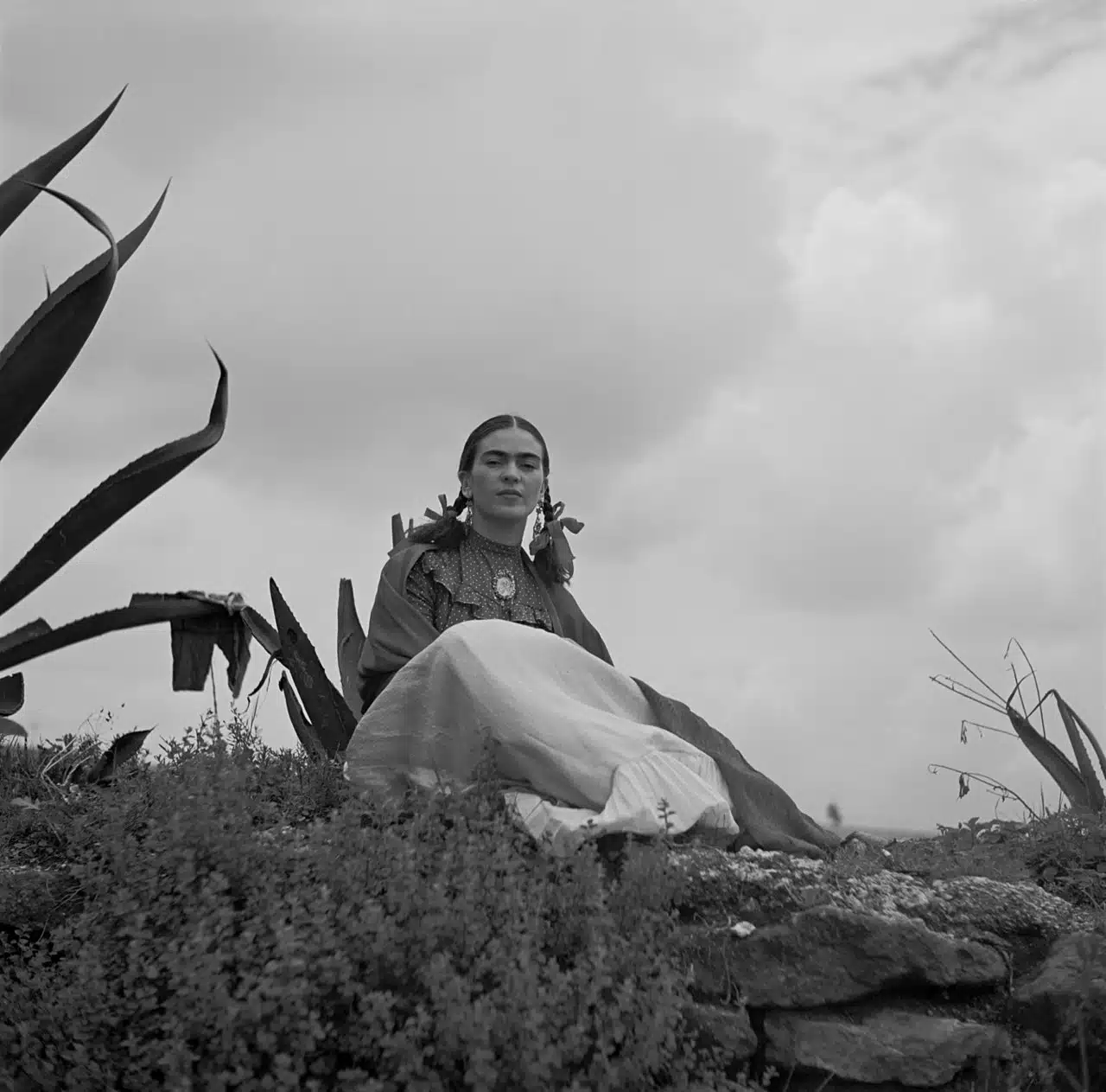 Historical photo of Frida Kahlo seated next to an agave plant.