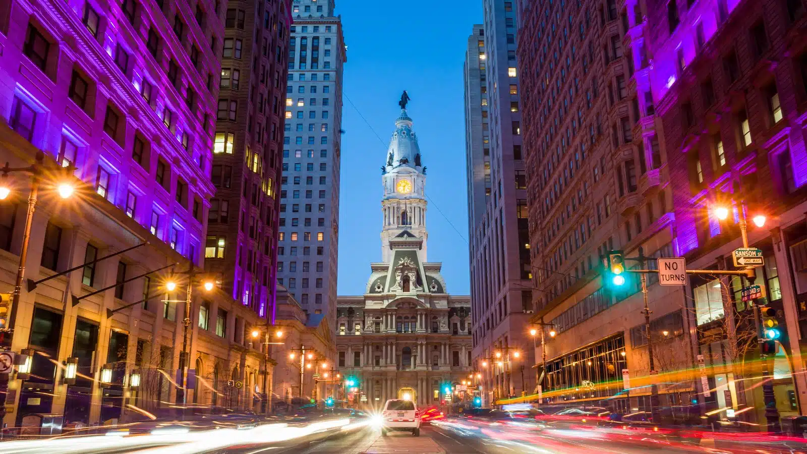 Philadelphia's City Hall as seen from down a bustling city street at dusk.