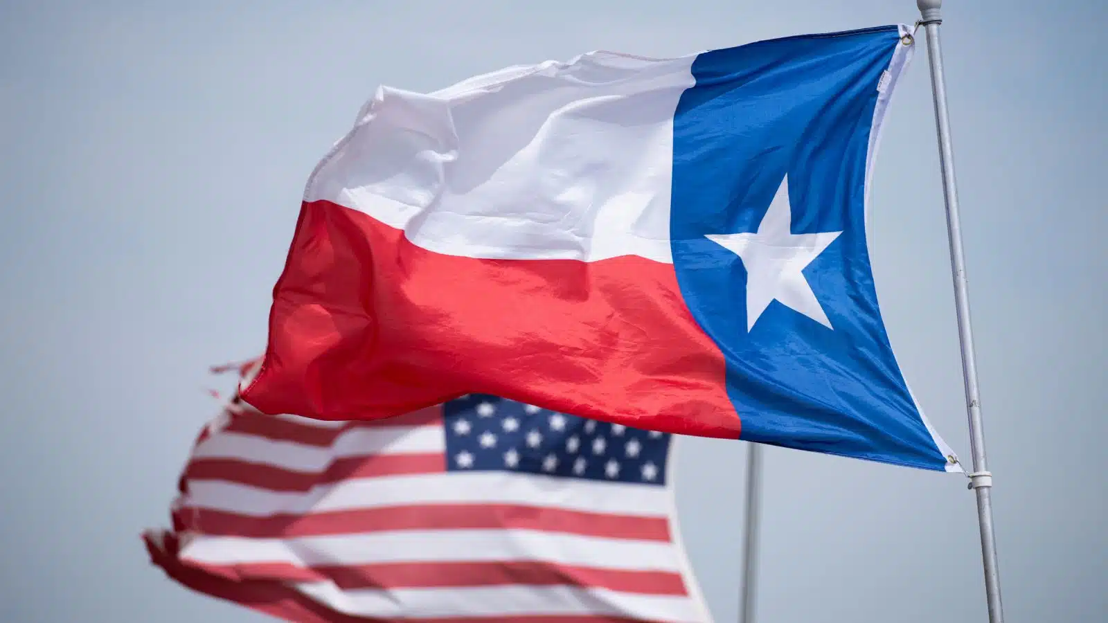 A Texan flag flying in front of a US flag.