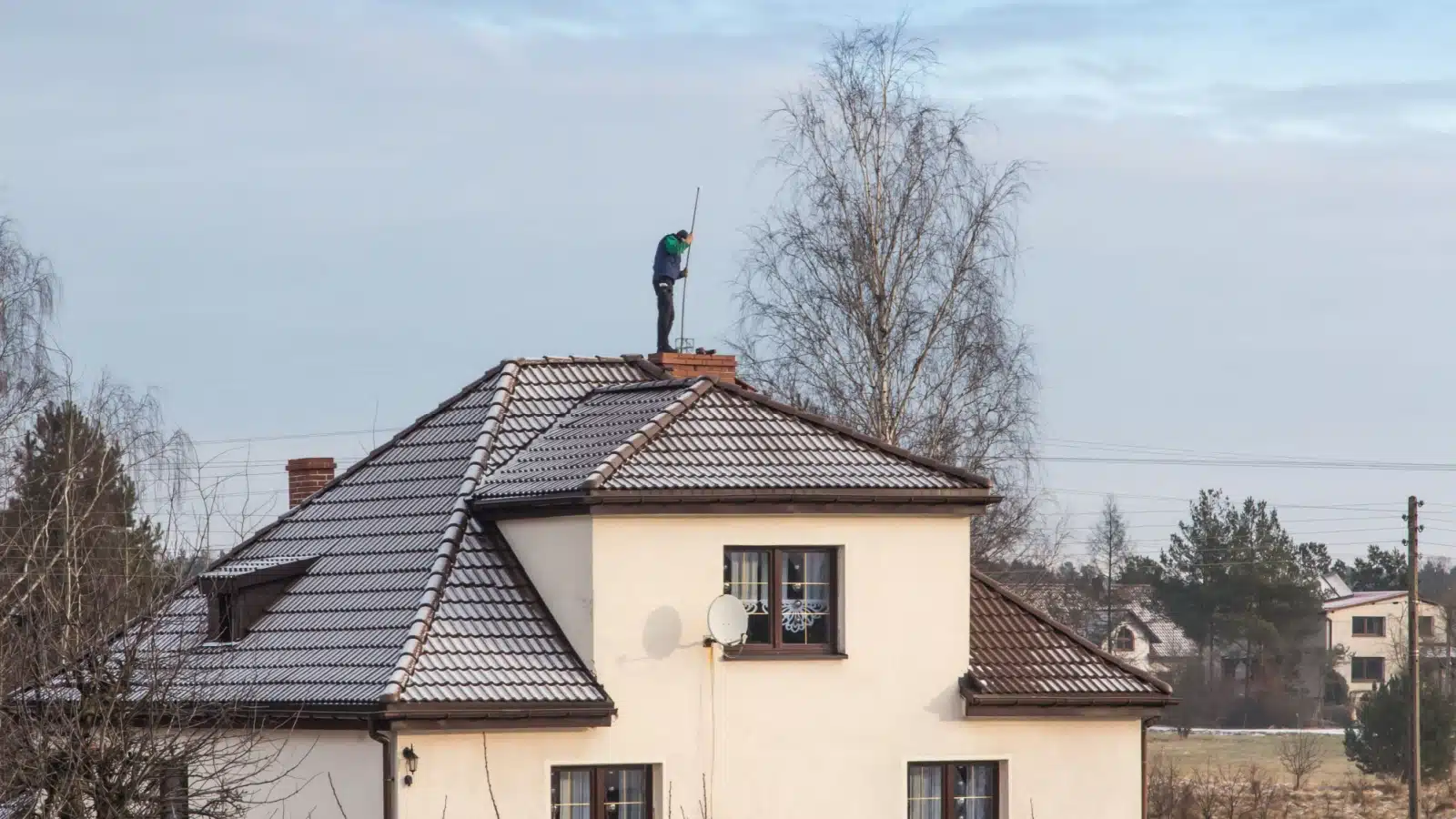 A chimney sweep on the roof cleaning a chimney.