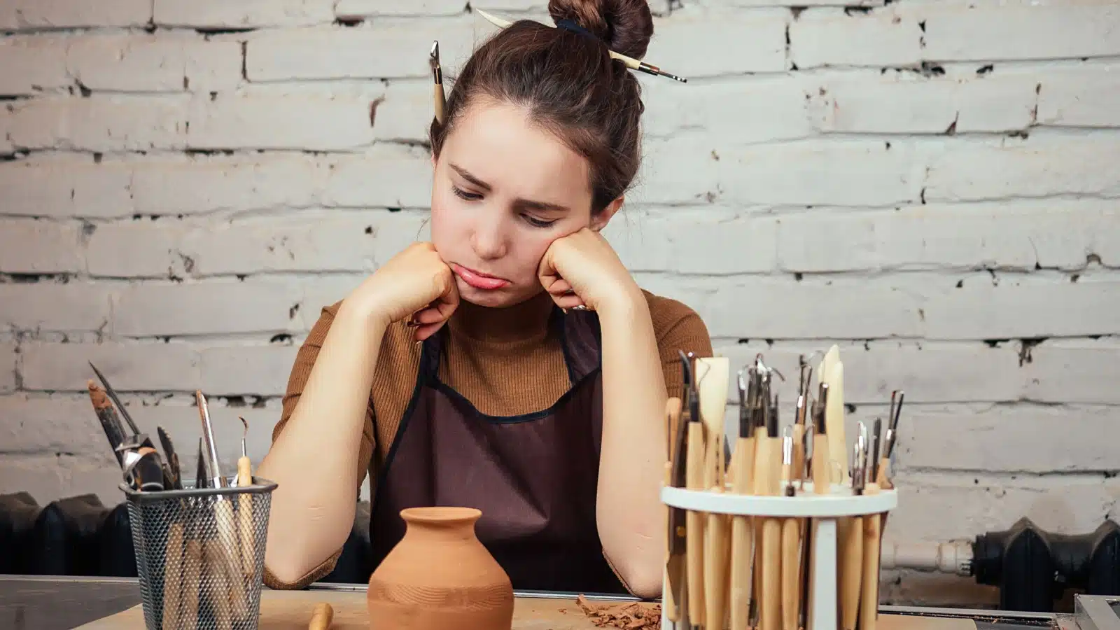 A woman looks sadly at her unfinished pottery, not feeling any passion for the project.
