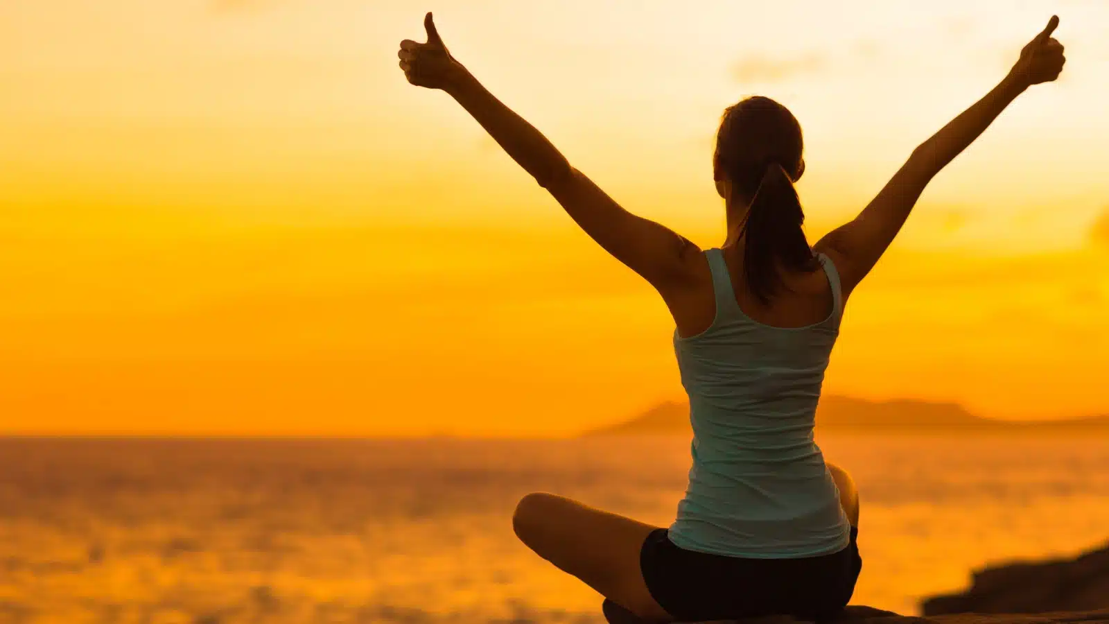 What is Passion? A woman sits at sunrise looking at the ocean with her arms in the air.