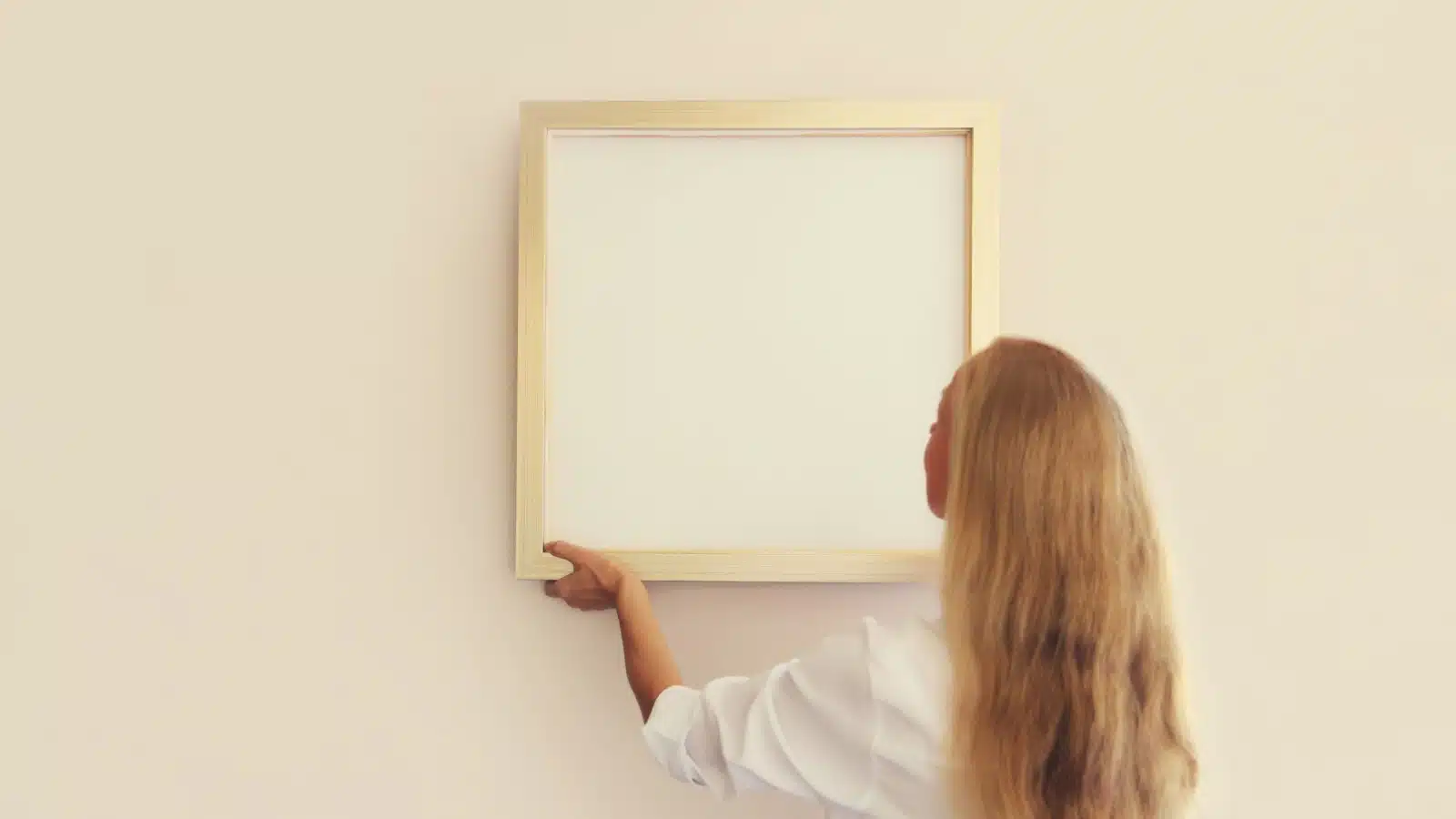 A woman hangs a blank frame.