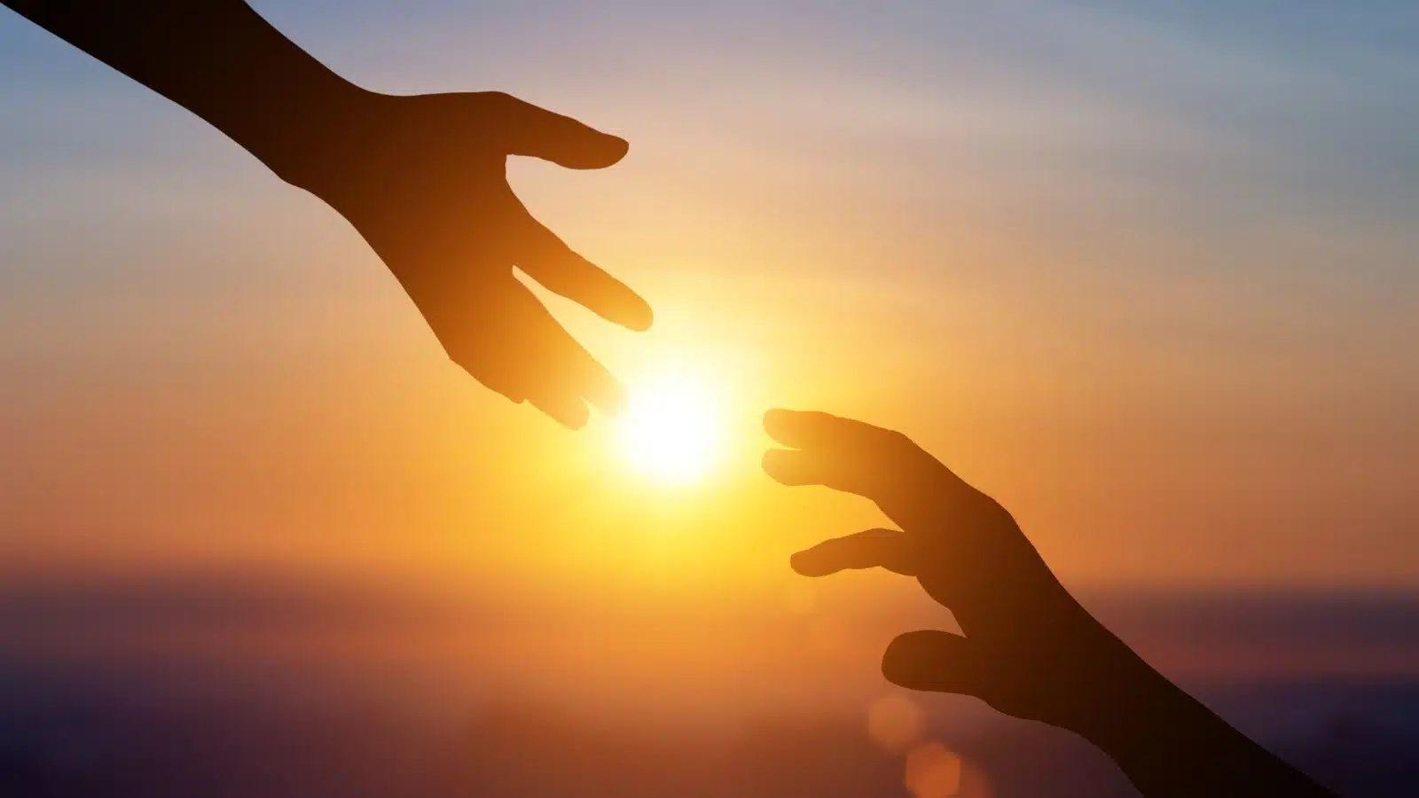 Close up of a hand reaching down to help another in the sunset to represent offering support or a helping hand.