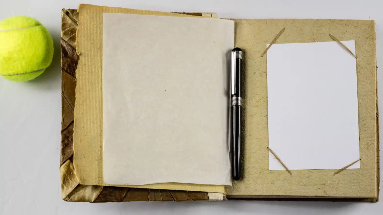 A home made junk journal sits on a table next to a tennis ball. 