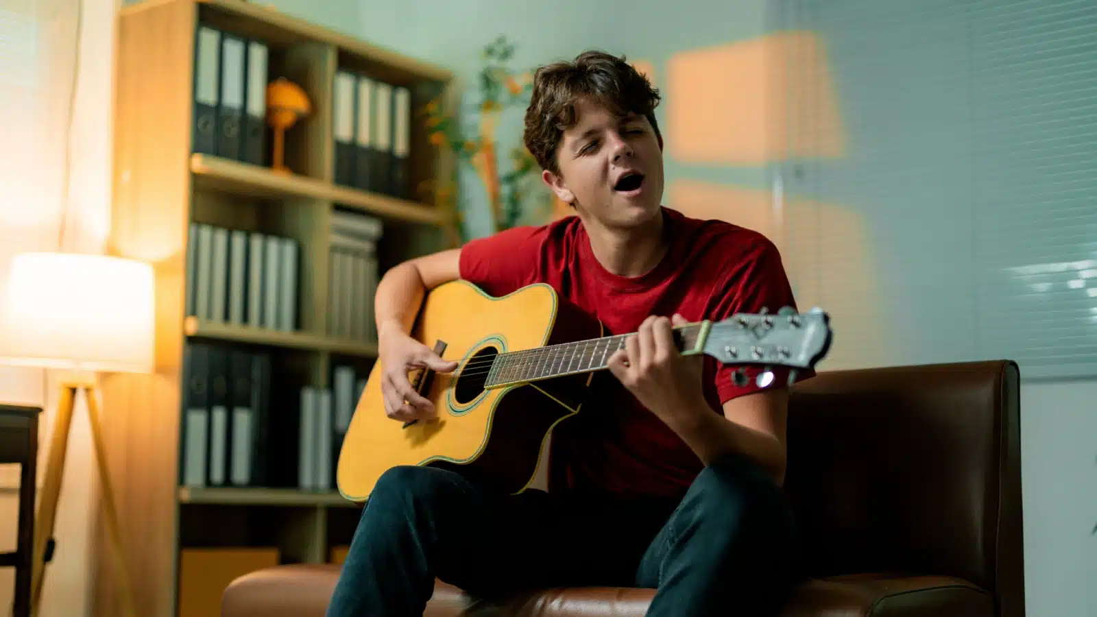 A young man sits on the couch playing guitar. You can tell that he's passionate about it from the joyful expression on his face.