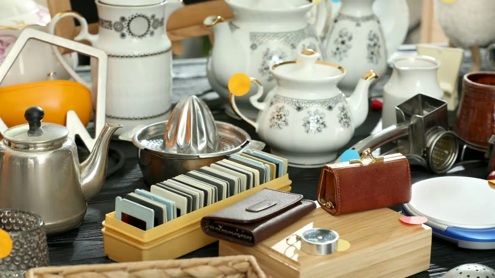 A table cluttered with random possessions like a teapot, wallet, and other random things.