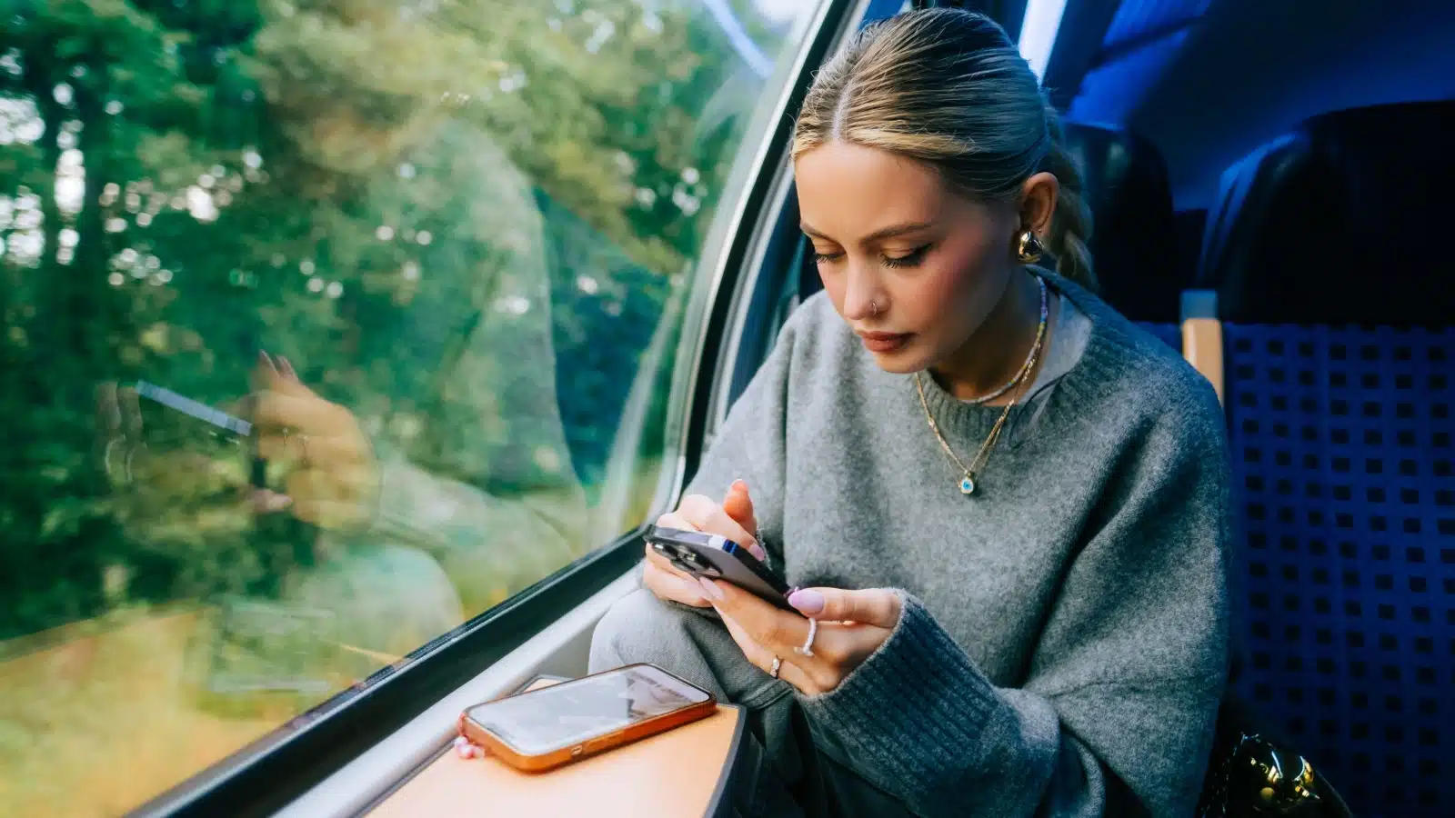 A woman rides a train while looking at her phone.