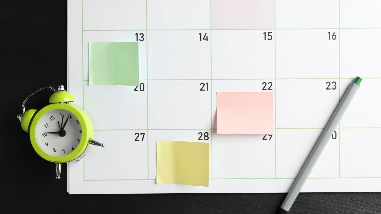 A calendar with post-it notes on certain days and a little alarm clock next to it.