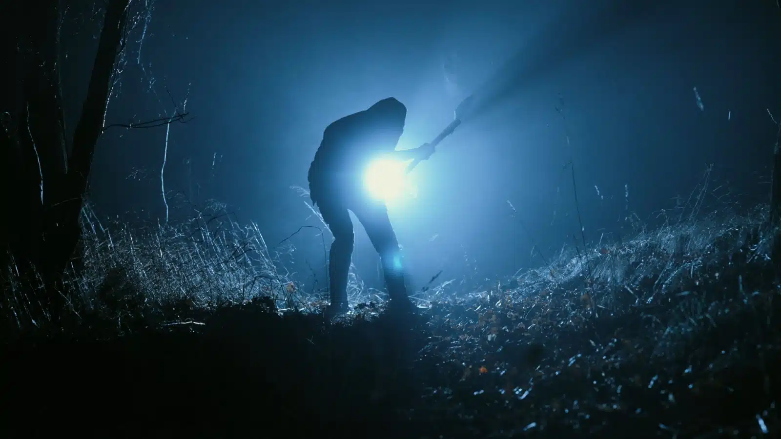 A figure holding a weapon shines a bright flashlight in the dark to represent disturbing unsolved mysteries. 