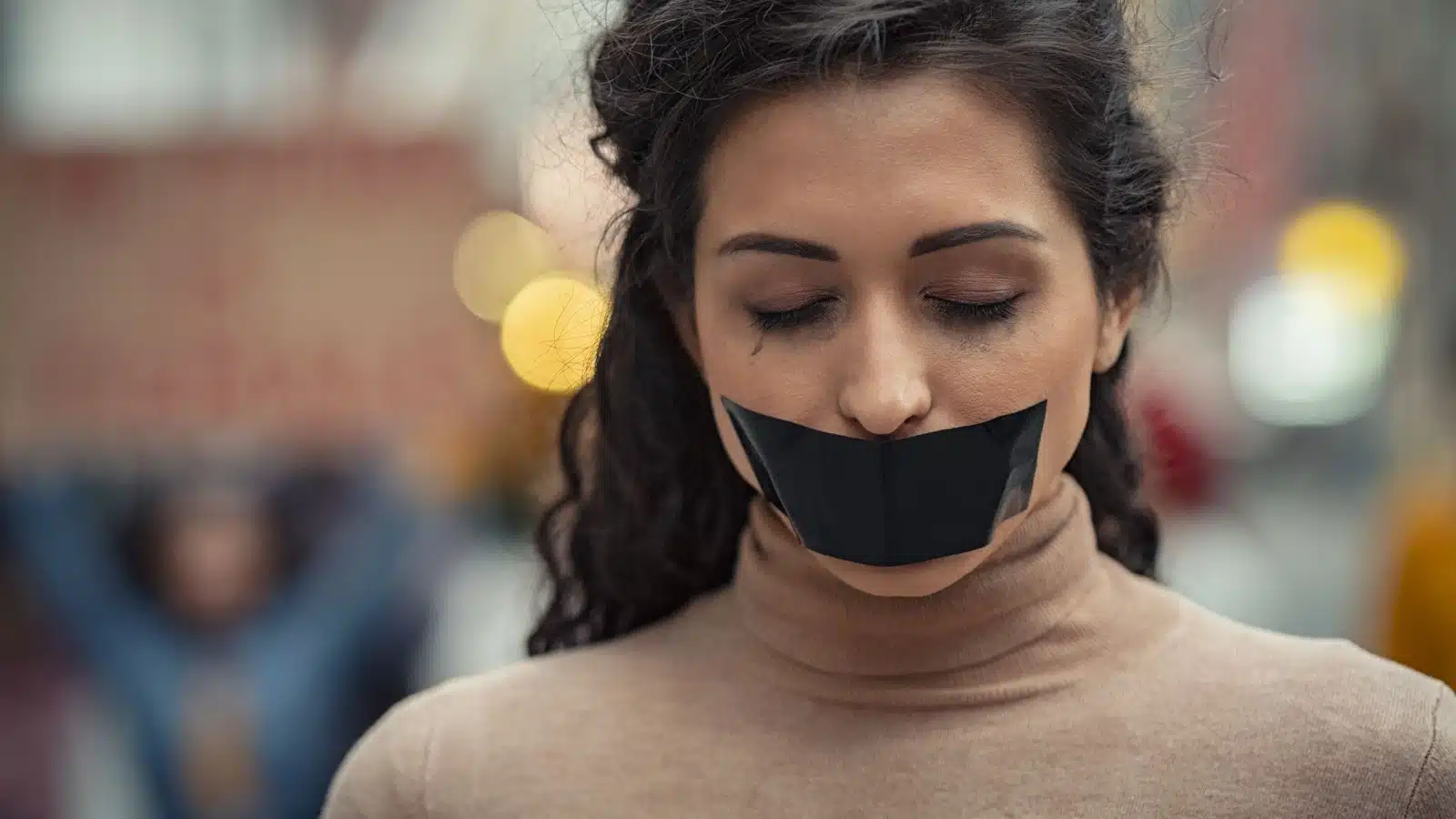 Portrait of a sad woman with black tape over her mouth to represent misogyny and sexism.