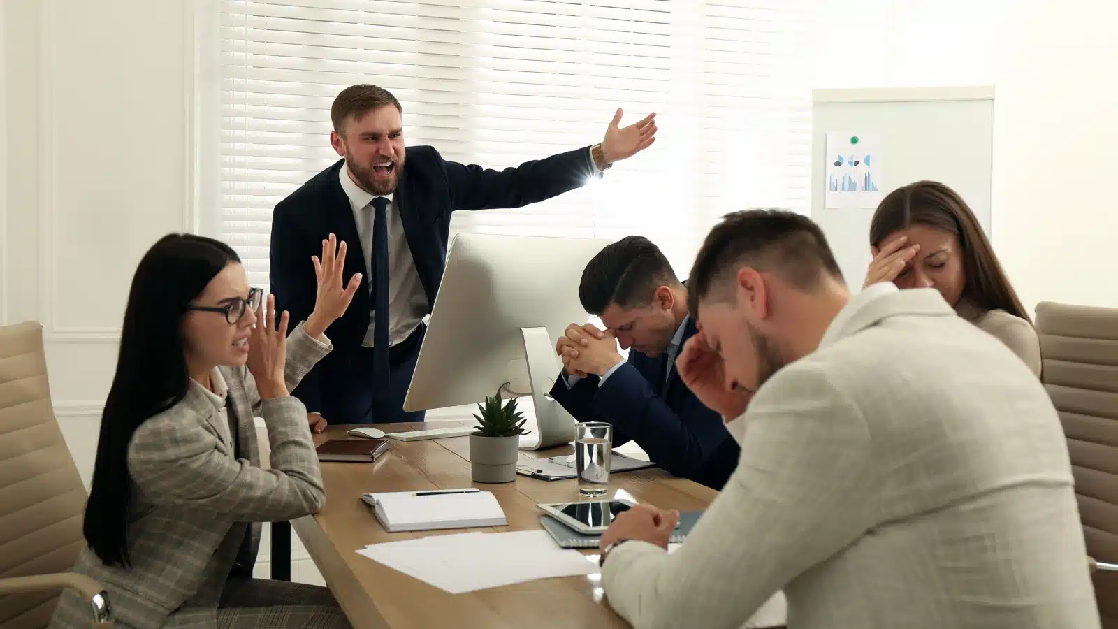 An angry boss yells at employees during a meeting.