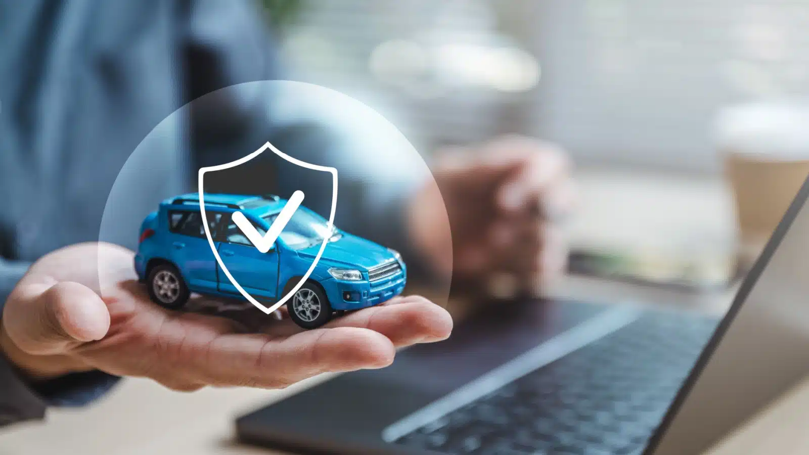 A person holds a model car in his hand that has a little security icon over it to represent car insurance.