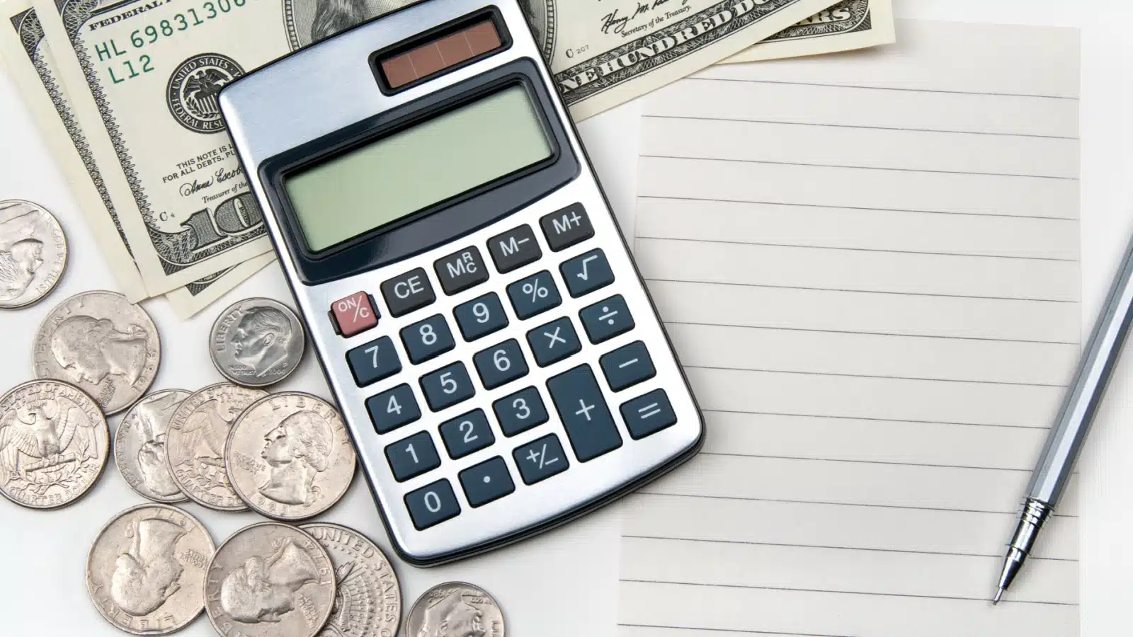 A calculator laying on money with pen and paper to represent the cost of living in 2022.