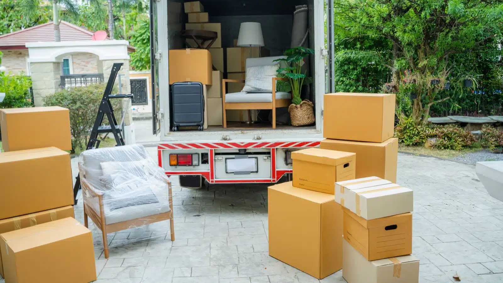 A moving truck half loaded surrounded by boxes on the ground.