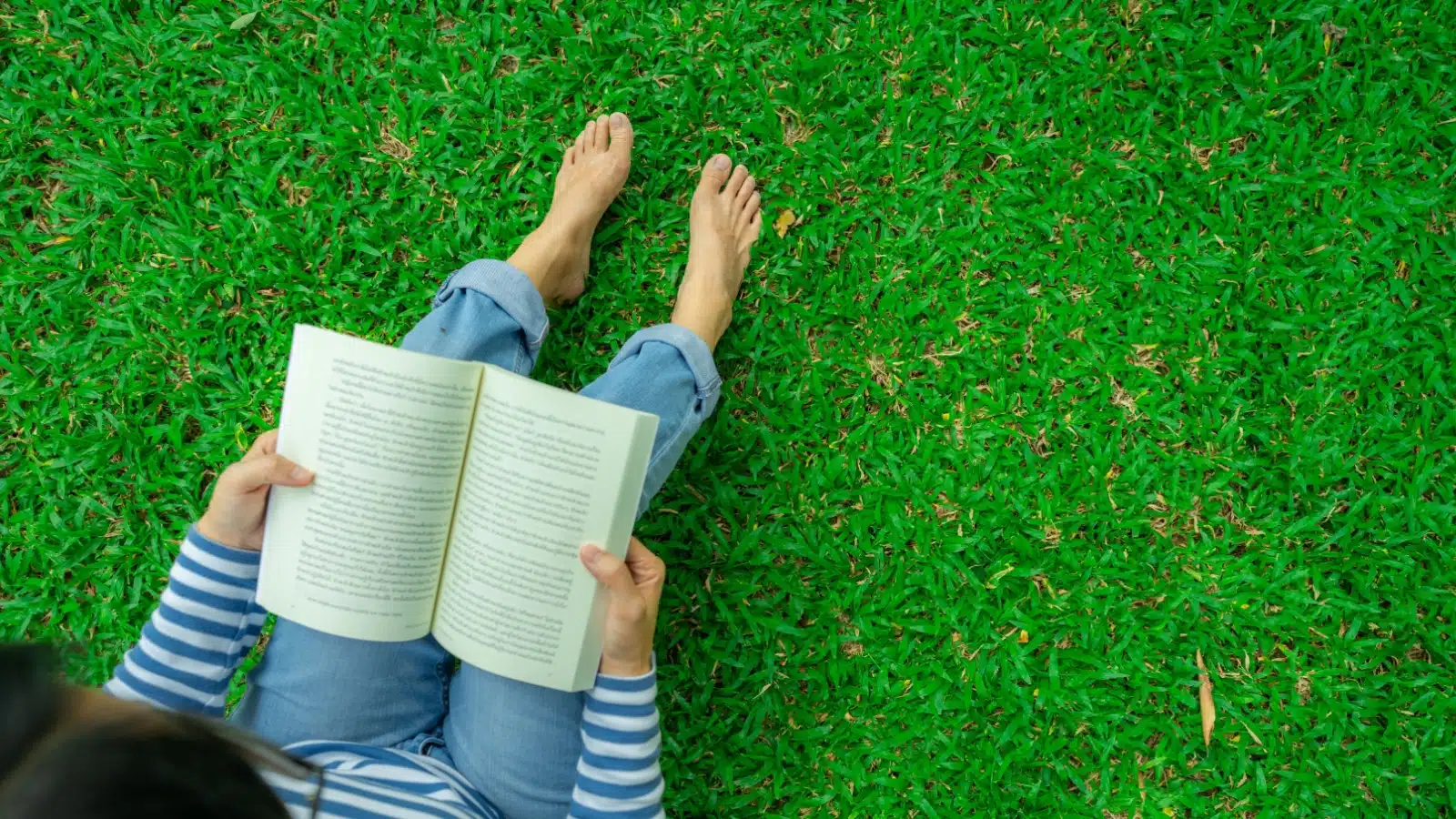A woman reads a book outside in the grass to represent free hobbies.