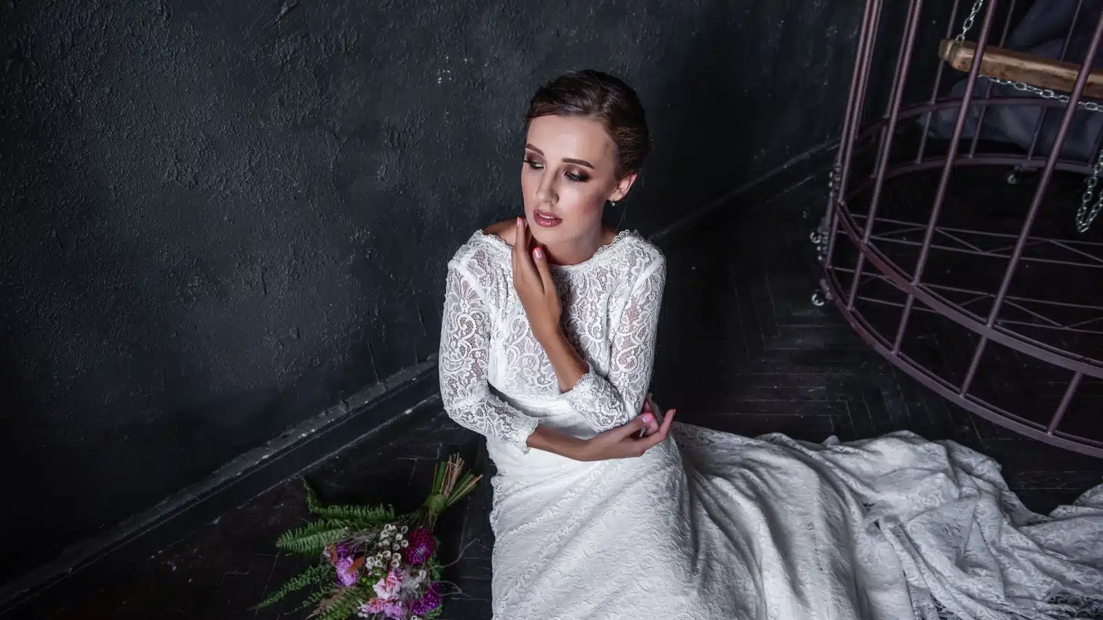 A sad, crying bride sits on the floor just outside an iron cage.