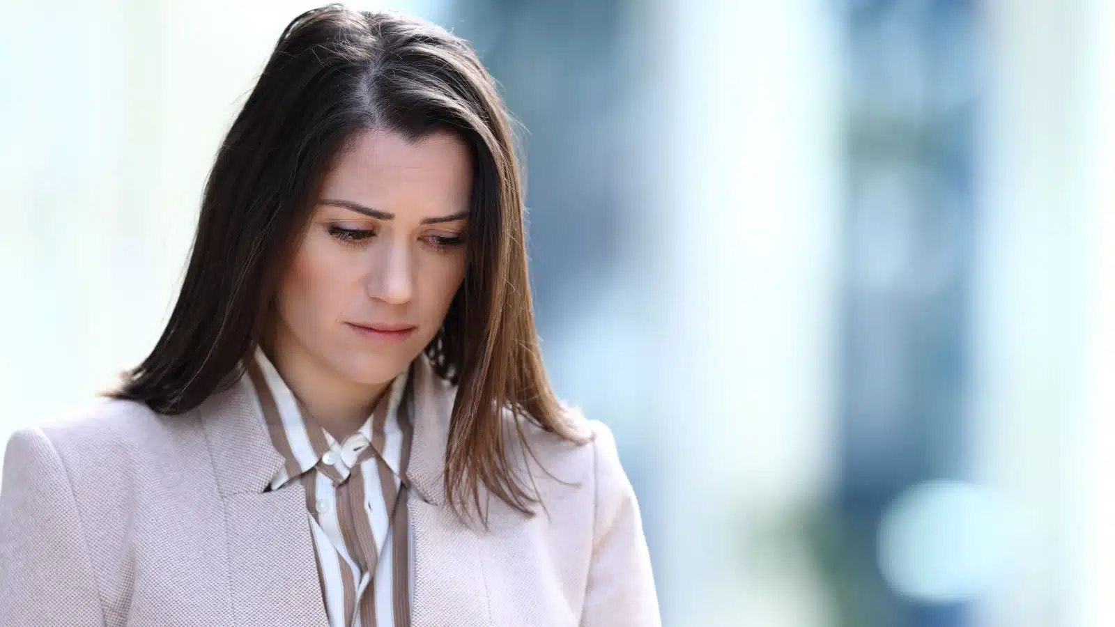 A sad looking woman struggling with self-doubt walks with her head down.
