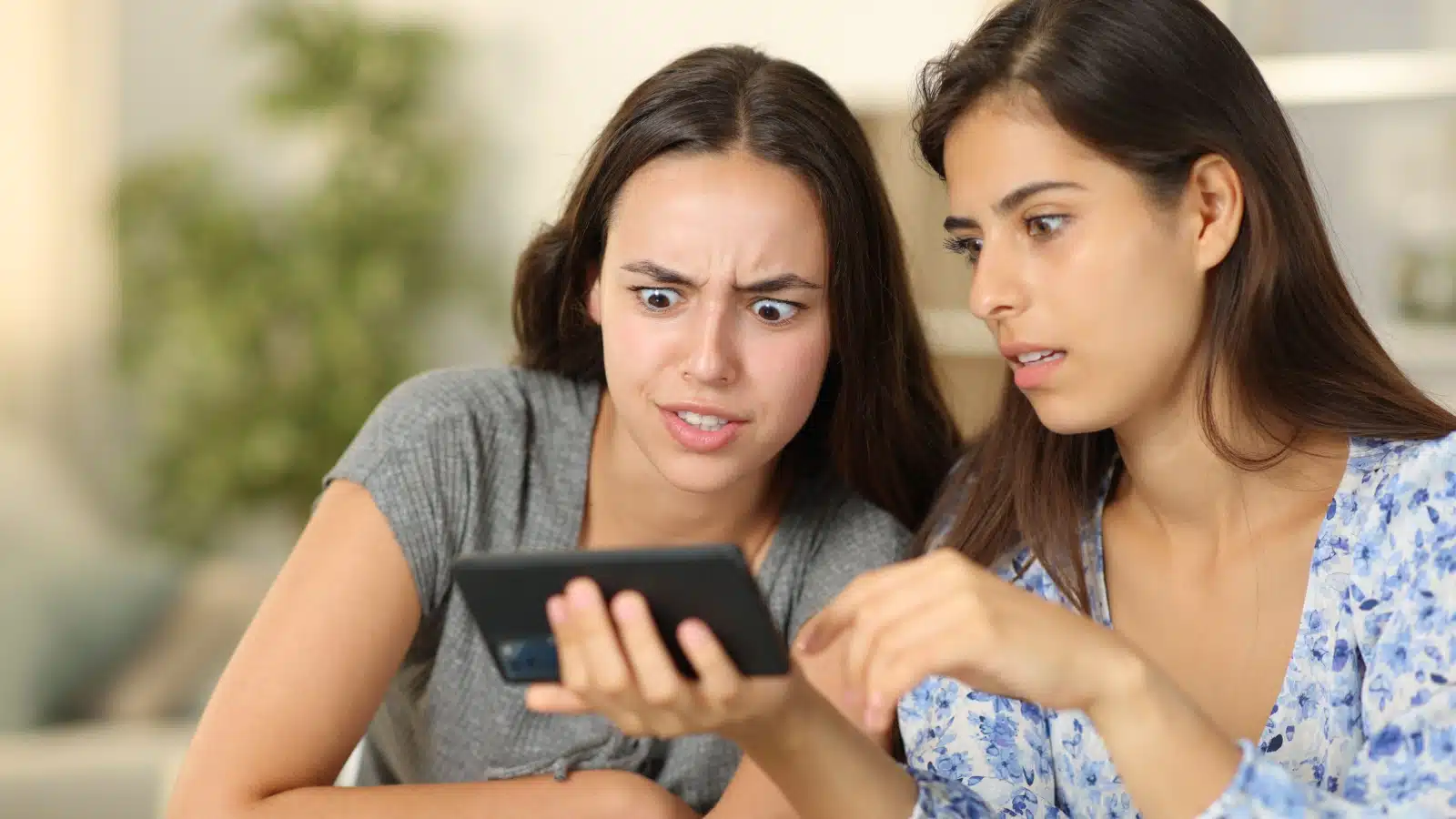 Two women look at a phone, disgusted by what they see, to represent things that turn women off. 