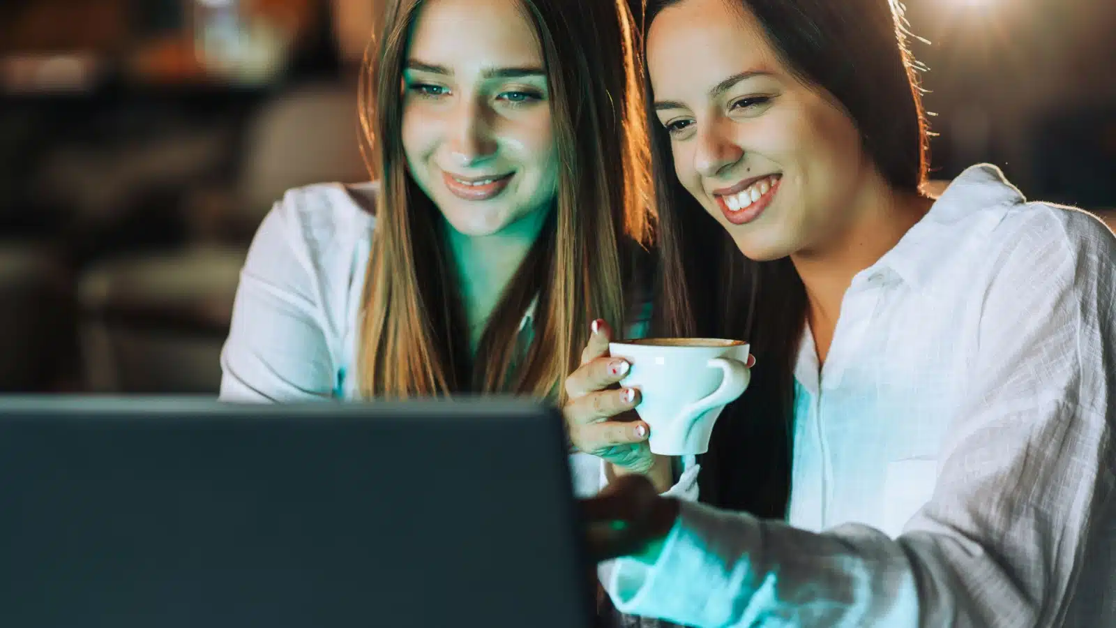 Two happy women using a laptop together visiting a website.