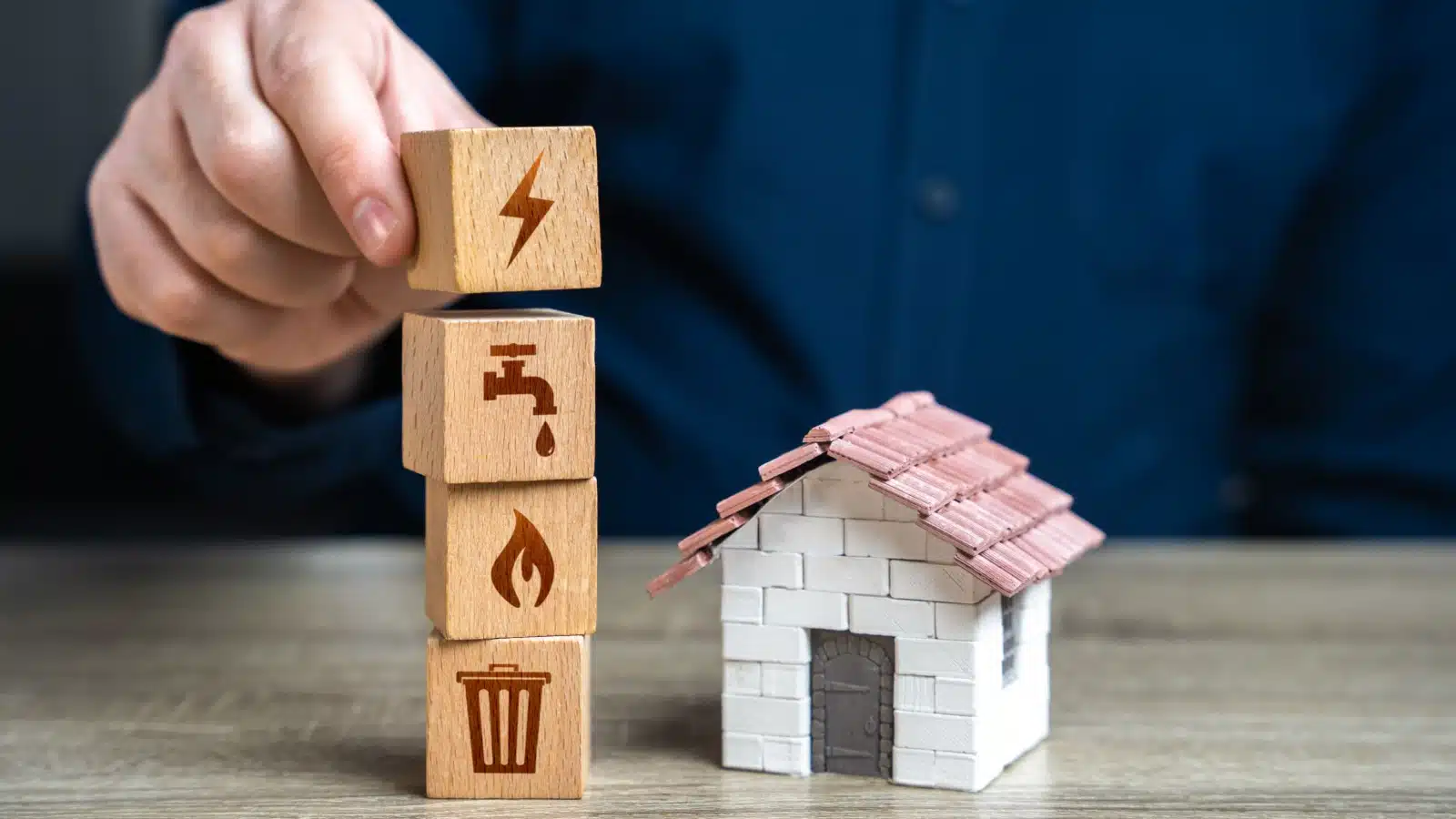 Wooden blocks with icons representing various utilities stacking next to a model house.