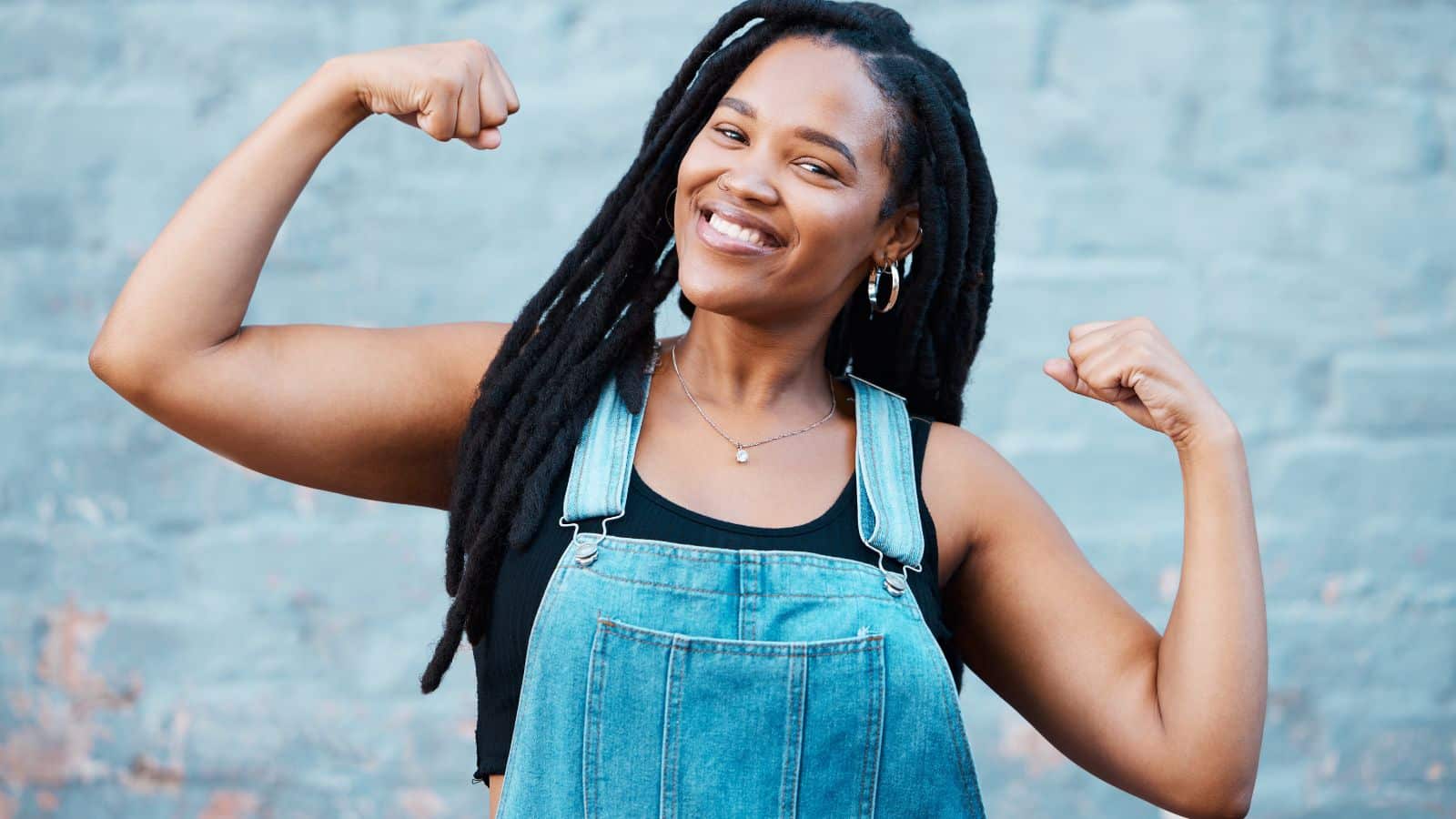 A smiling woman poses with her arms raised, flexing her biceps to showcases that you are stronger than you think.